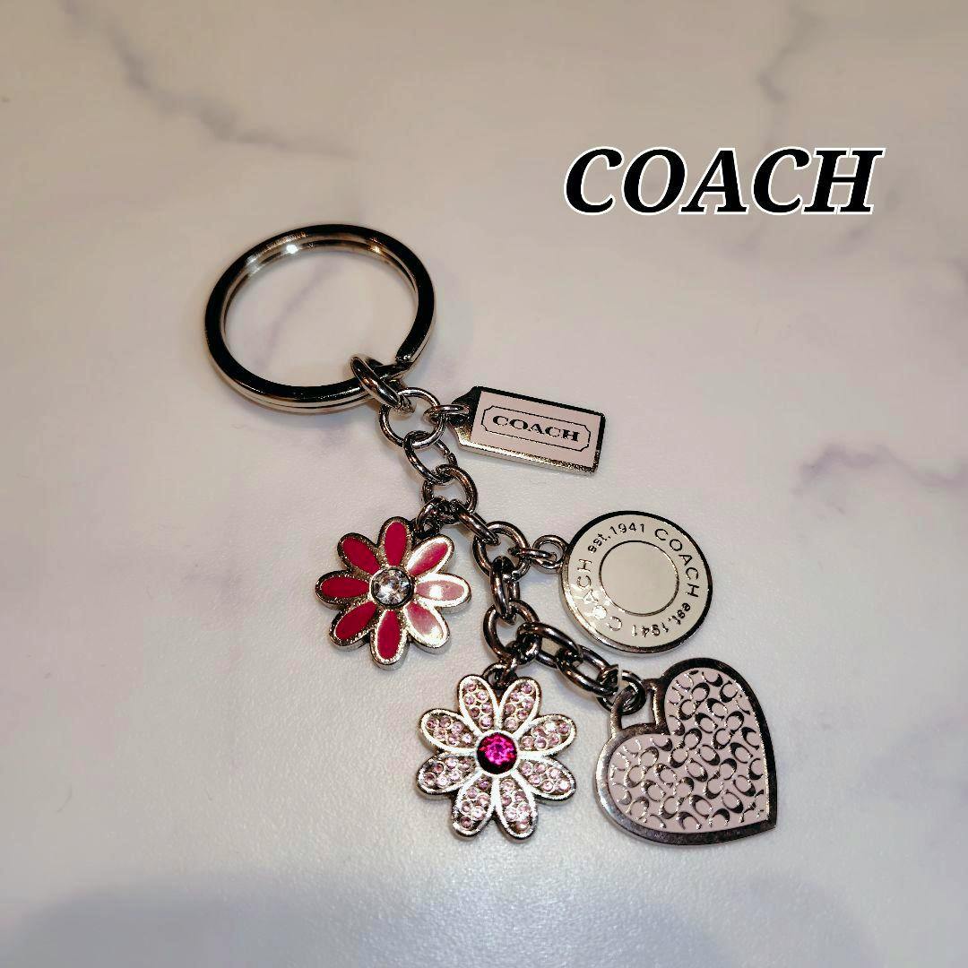 COACH bag charm keyring with pink flower, jeweled flower, round tag, and heart charm on a light background.