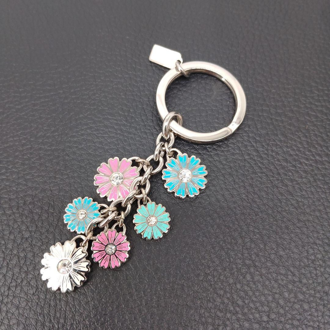 Multicolor COACH flower keychain with several enamel daisy charms on a silver-tone key ring shown on a black textured background.