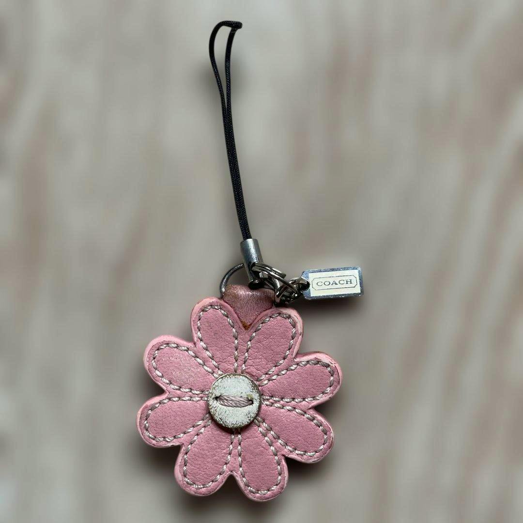 Pink leather flower-shaped COACH keychain with stitched petals, a central button detail, and a small metal COACH tag attached.