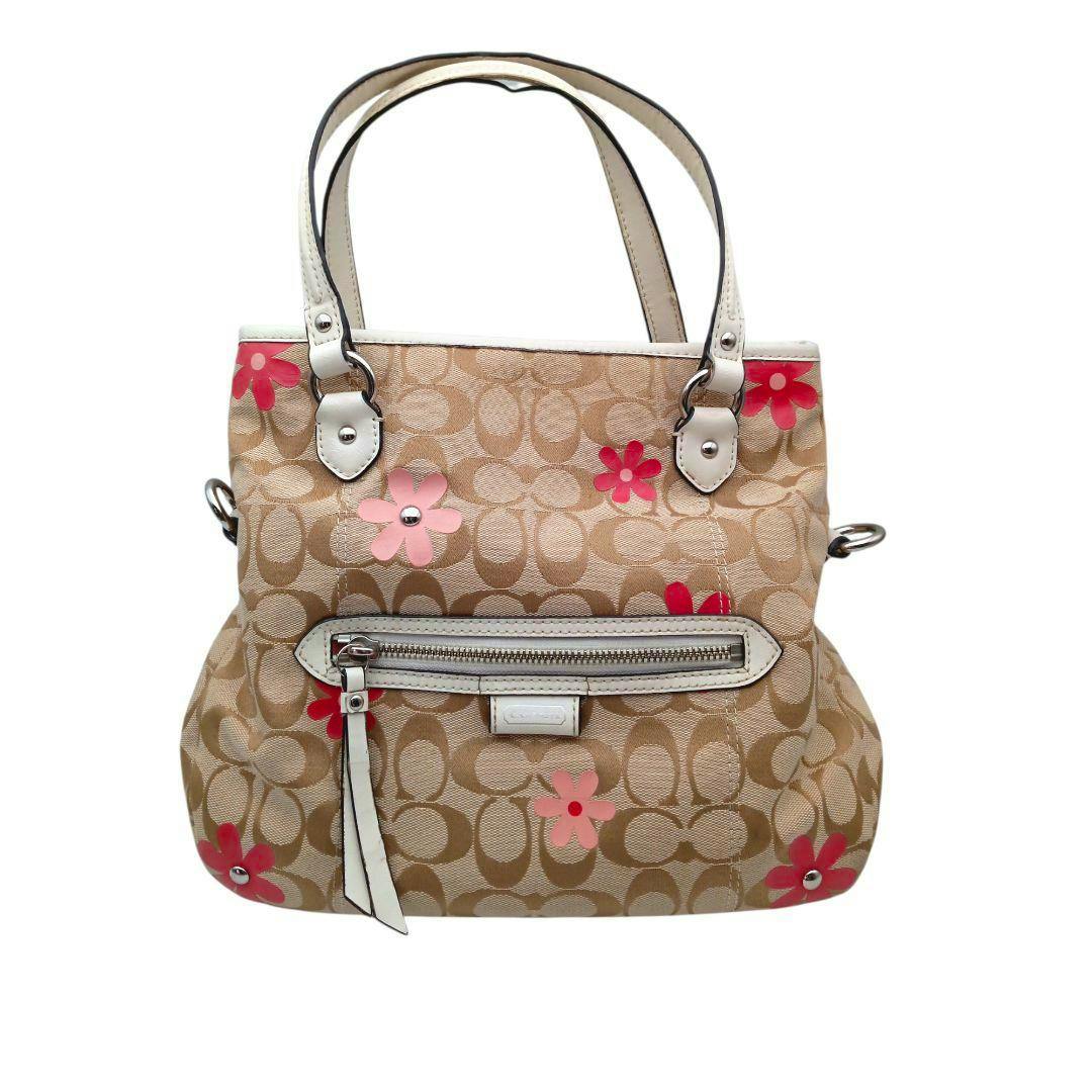 Front view of a Coach canvas tote bag with floral print, white handles, and a front zip pocket.