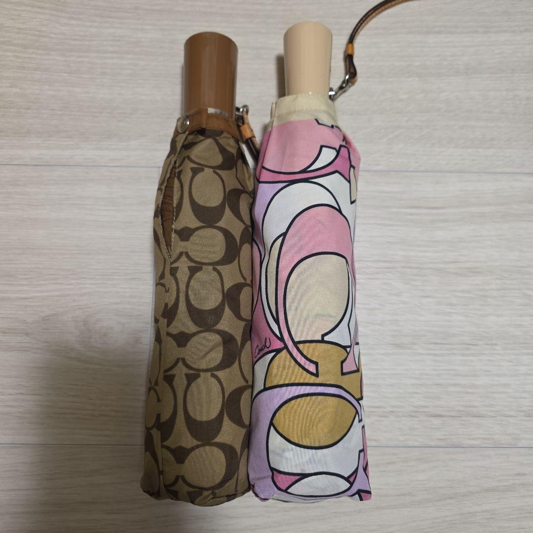 Two folded umbrellas in fabric sheaths, one brown patterned and one pink patterned, side by side on a light surface.