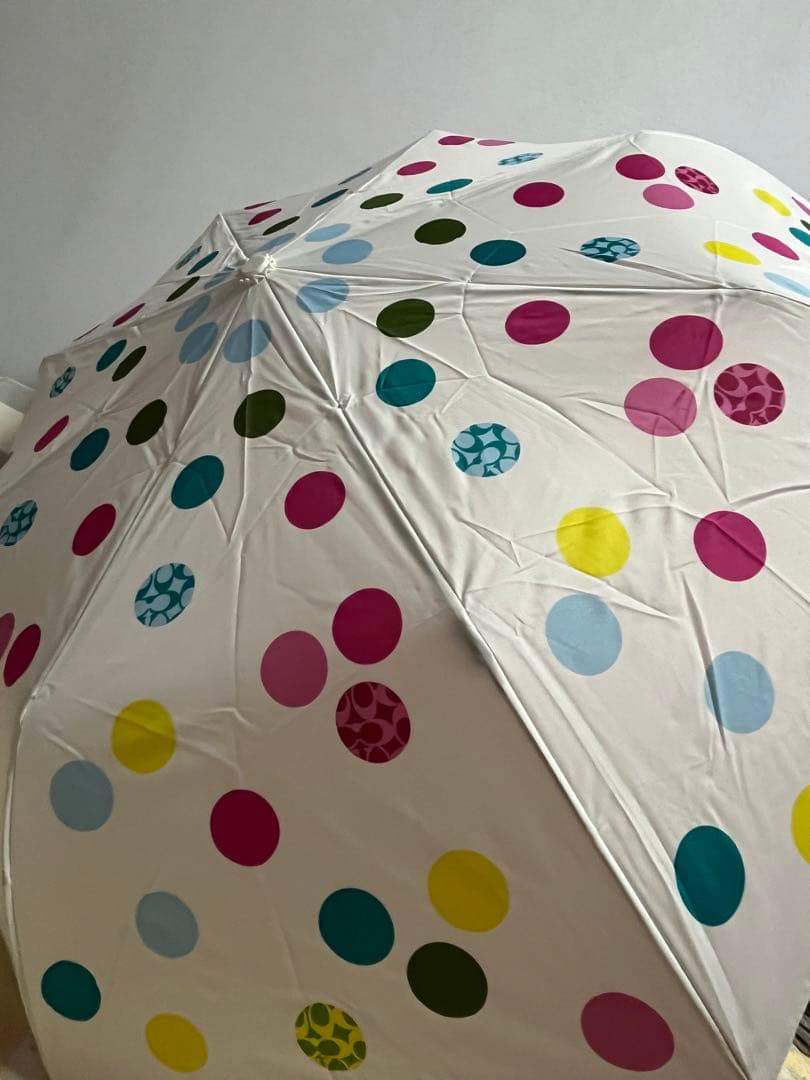 White foldable umbrella with multicolored polka dots shown from an angled exterior view.