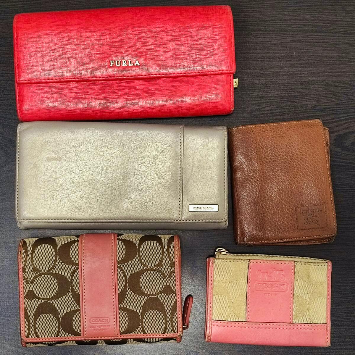 Five wallets and coin cases laid flat on a dark surface, including a red Furla long wallet and a Coach signature canvas wallet.