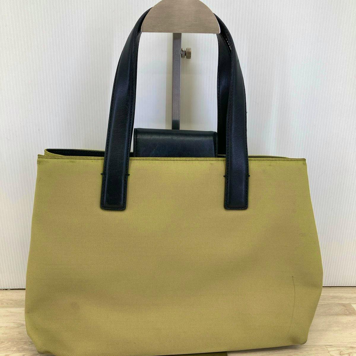 Front view of a beige twill tote bag with black leather handles.