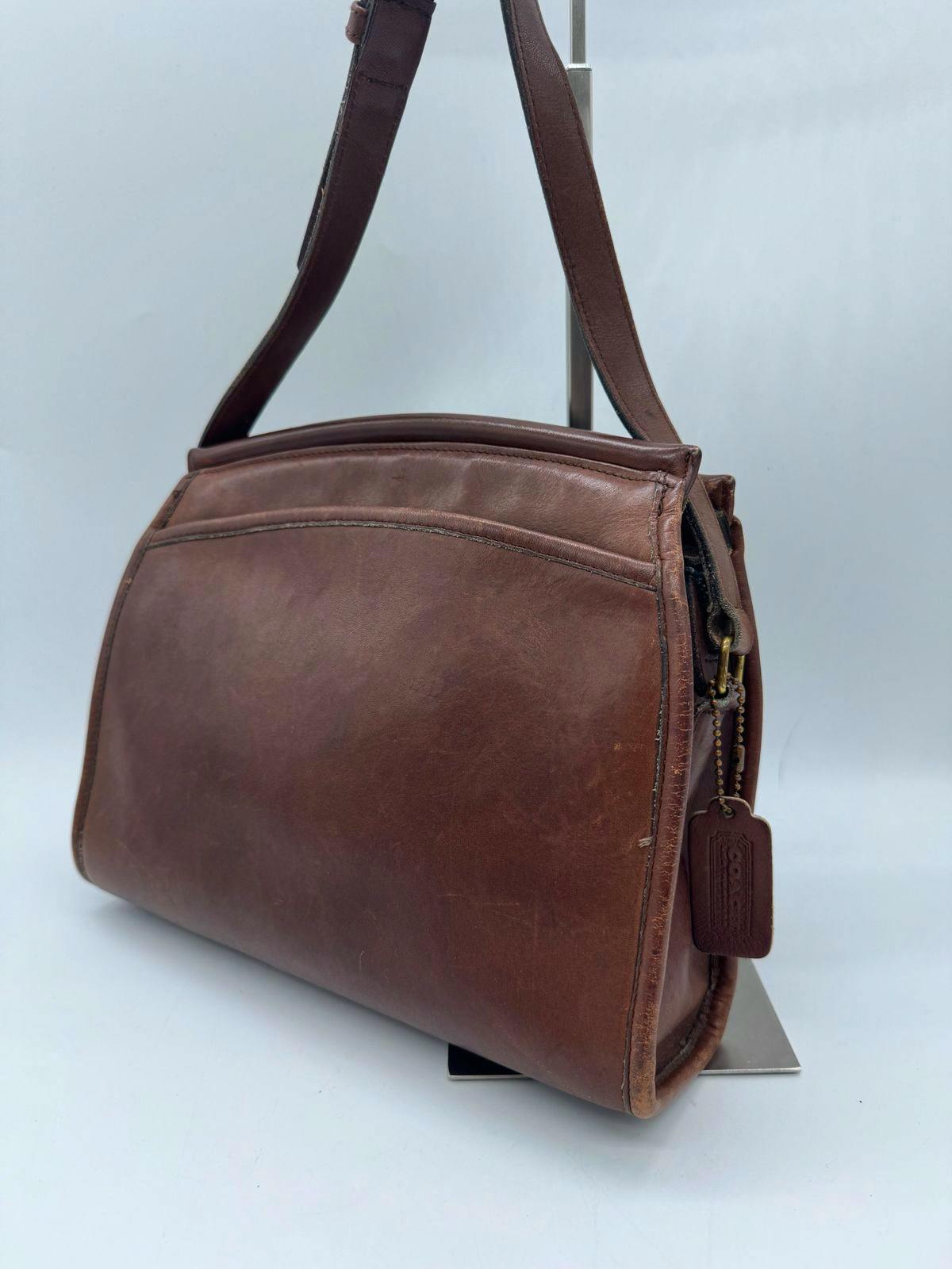 Brown COACH cow-leather shoulder bag with strap and a hanging leather tag shown from a side angle.