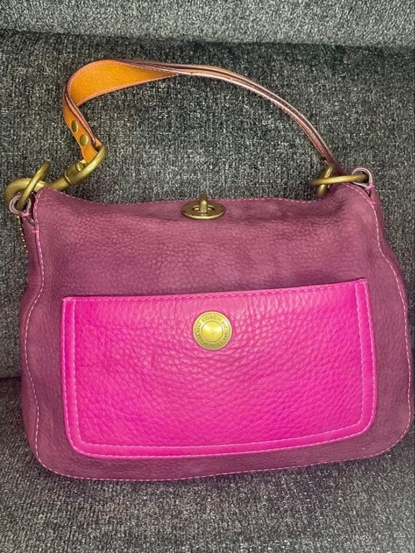 Front view of the Coach goat leather shoulder bag showing a maroon body, bright pink front pocket, brass turn-lock, and tan leather strap.