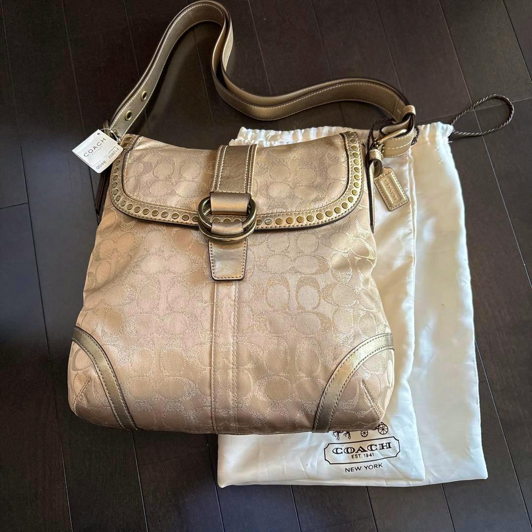 Gold COACH canvas shoulder bag with flap and buckle, shown on a COACH dust bag.