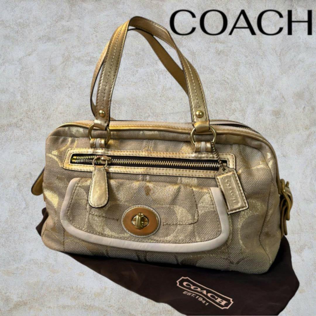 Gold Coach canvas handbag with a front turn-lock pocket and two top handles shown on a Coach dust bag.
