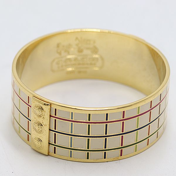 Gold-colored metal bracelet bangle with multicolored enamel grid pattern photographed on a white background.