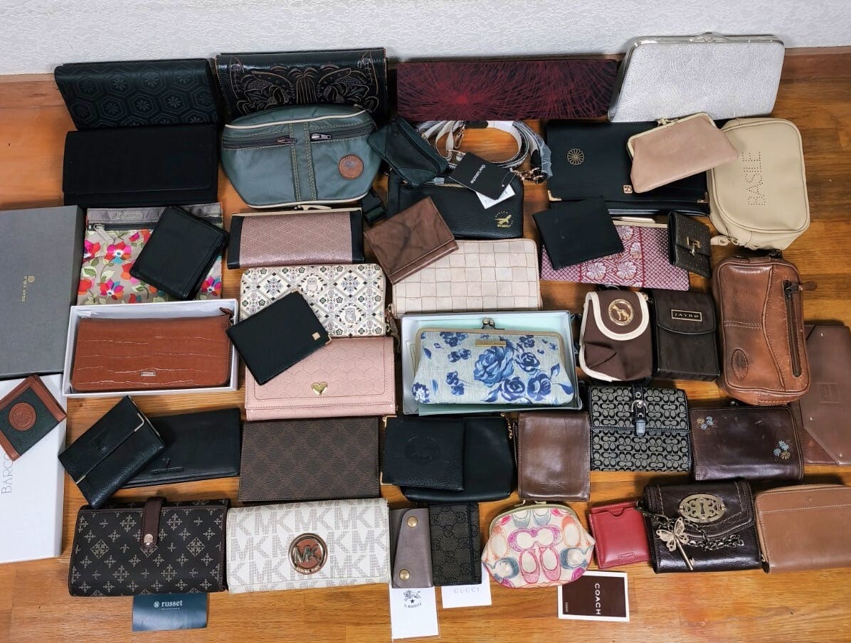 A large assortment of wallets, long wallets, coin purses, and pouches arranged on a wooden floor.