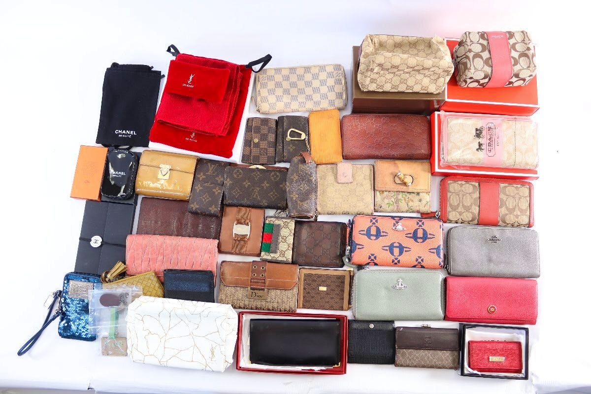 Overhead photo of a large assortment of wallets, pouches, and small accessories laid out on a white background.