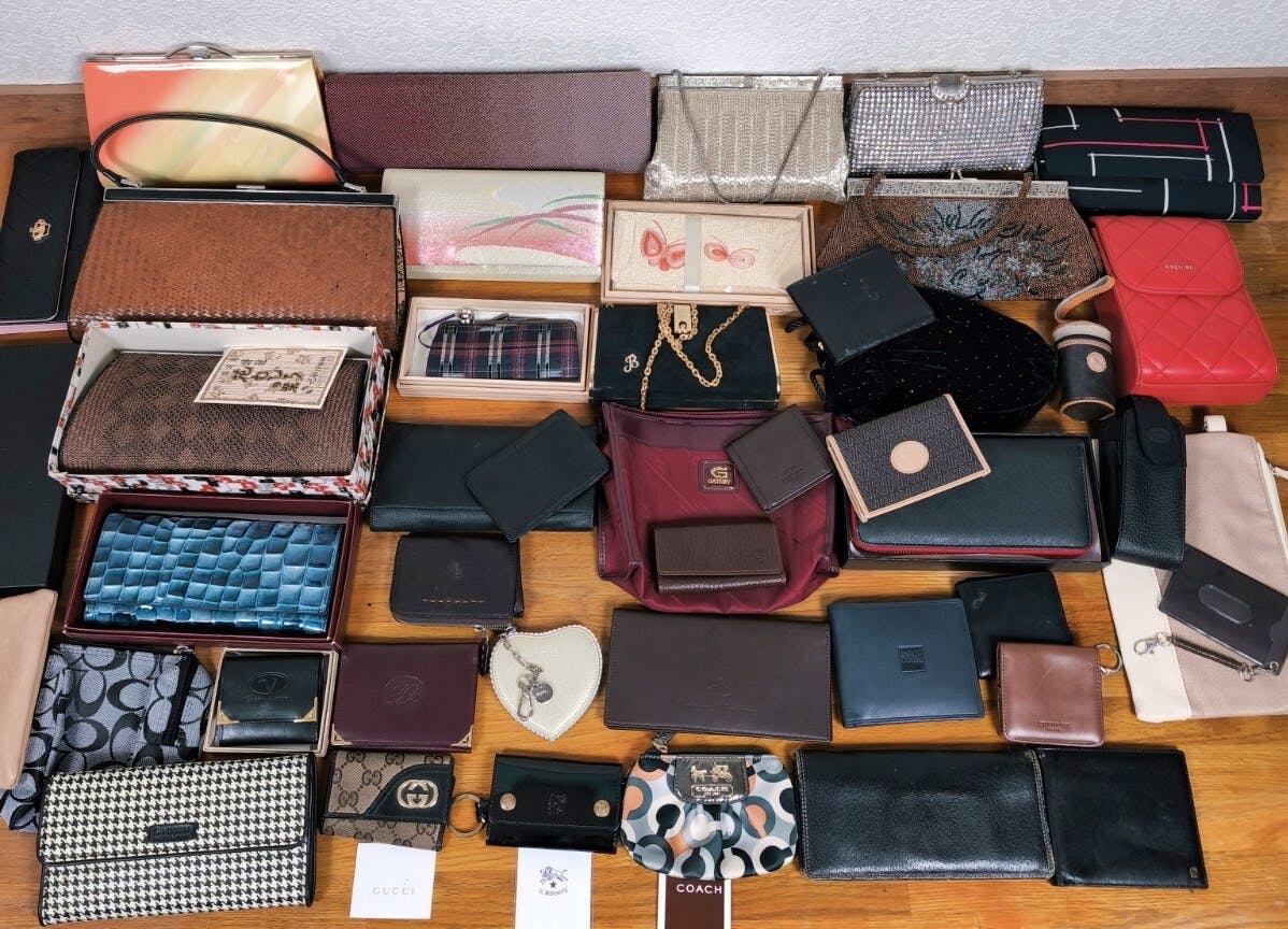 A large assortment of wallets, pouches, and small bags arranged on a wooden floor.