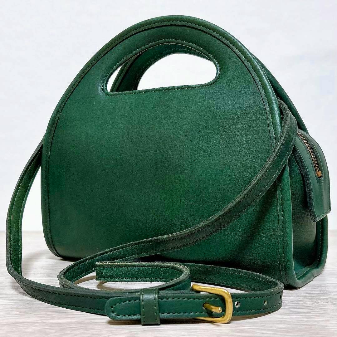 Green Coach half-moon cow leather shoulder bag with a top handle cutout and an adjustable green leather shoulder strap with a gold-tone buckle.