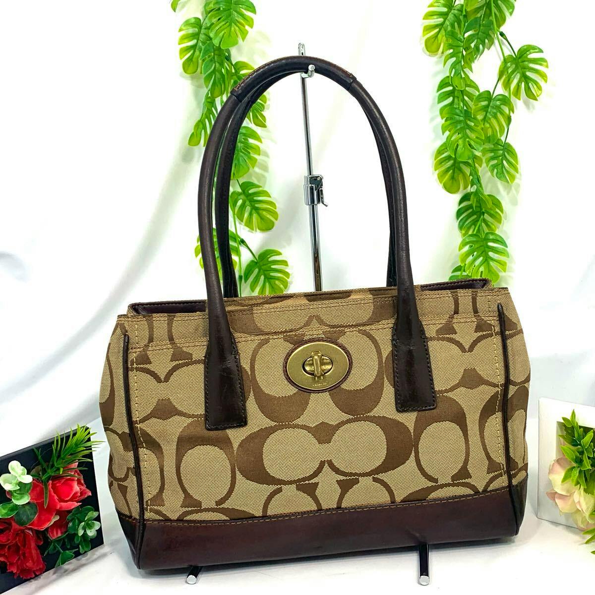 Brown Coach Hampton signature canvas handbag with turn-lock closure and leather handles displayed on a stand.