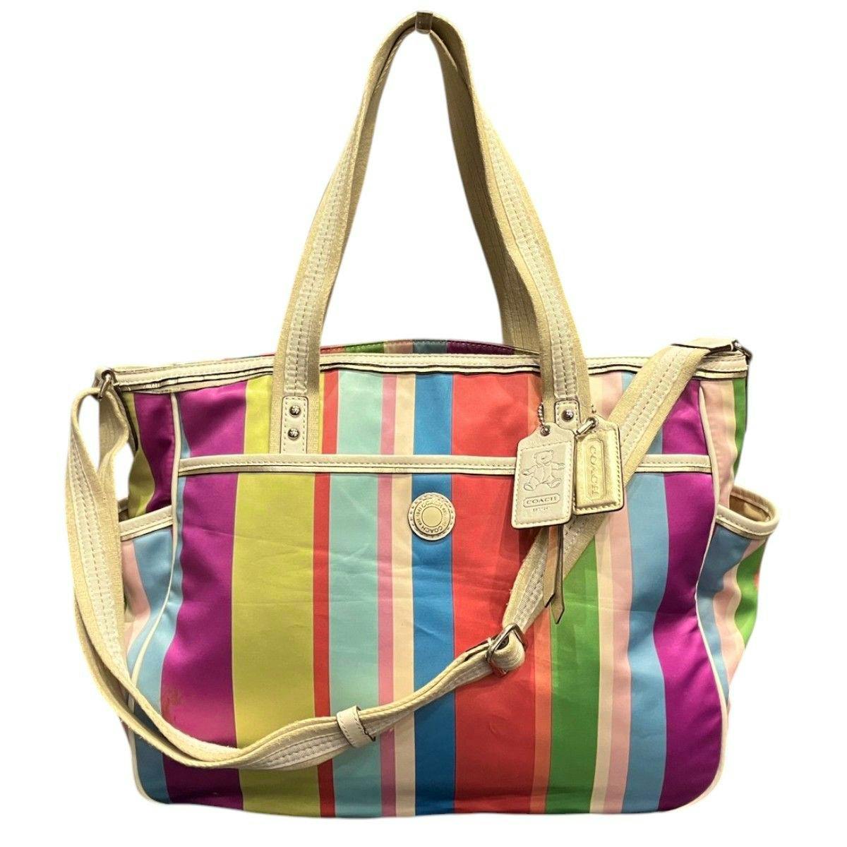 Front view of a multicolored striped Coach tote bag with cream leather handles, shoulder strap, and brand tags.