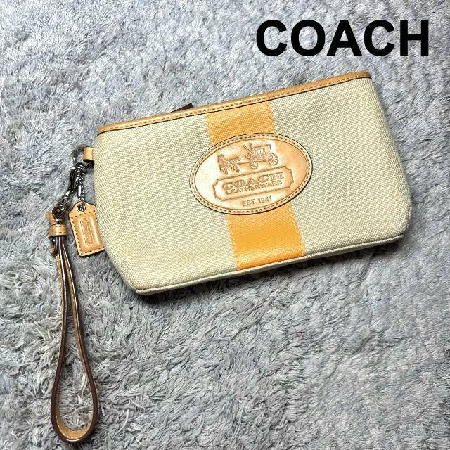 COACH canvas wristlet pouch in beige with an orange center stripe and leather logo patch on a gray rug.