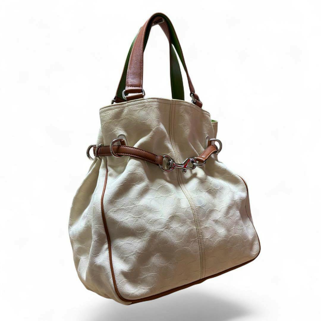 White Coach Hamptons carryall bag with brown handles, green interior, and silver hardware on a white background.