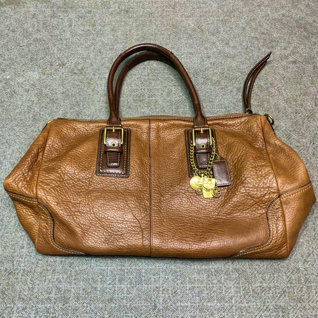 Brown Coach leather satchel with double top handles and a gold charm, shown lying flat.
