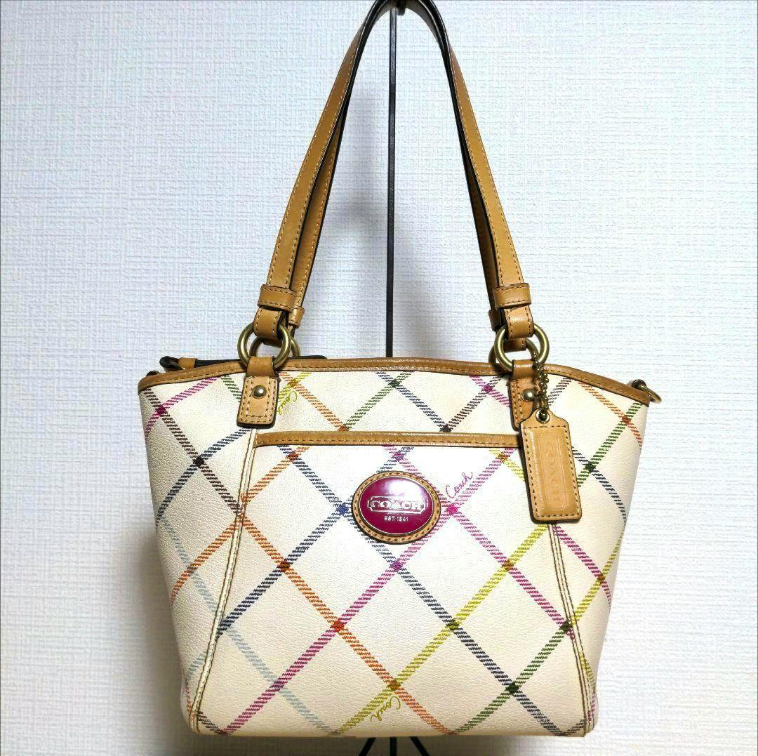 White Coach handbag with multicolored diagonal plaid pattern and tan leather handles and tag.