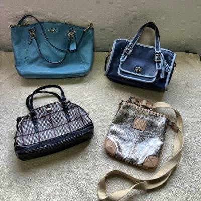 Four handbags arranged on a light surface: a light blue tote, a navy shoulder bag, a plaid small bag, and a metallic crossbody bag.