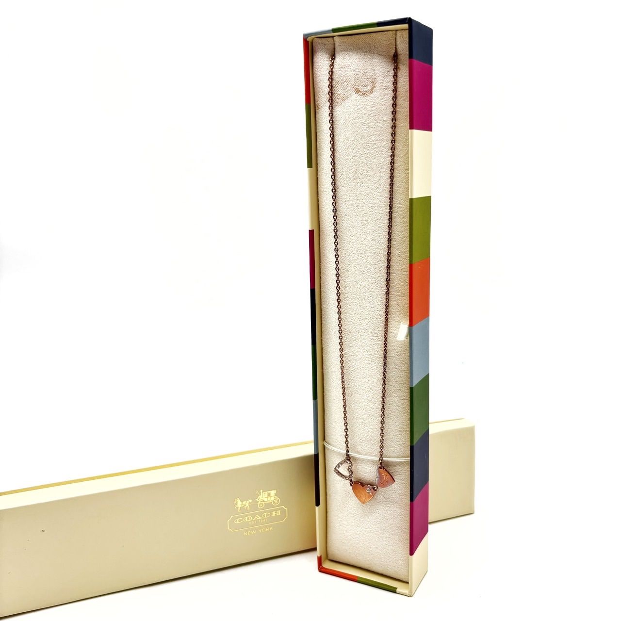 A Coach heart chain necklace with multicolored heart pendants displayed inside its box.