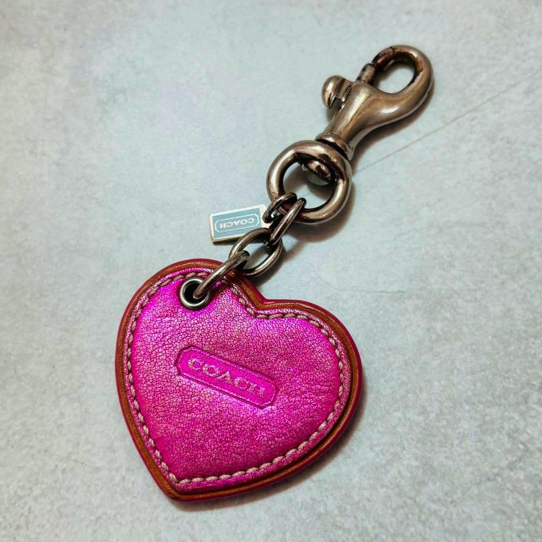 Pink heart-shaped COACH keychain bag charm showing the front embossed COACH logo with metal clasp and small tag.