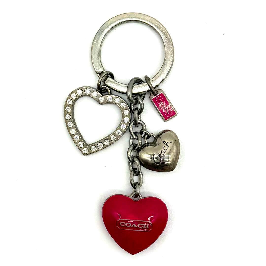 Coach heart-motif key ring bag charm showing a silver-tone split ring with a rhinestone open-heart charm, a small engraved metal heart, and a red enamel heart stamped "COACH".