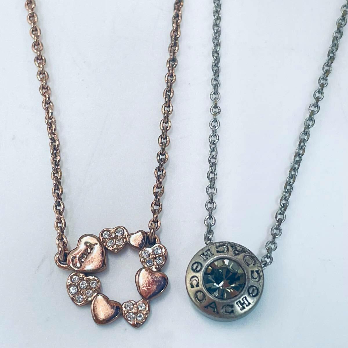 Two necklaces on a white background: a pink-gold open-heart circle pendant with clear stones and a silver round Coach pendant on chains.