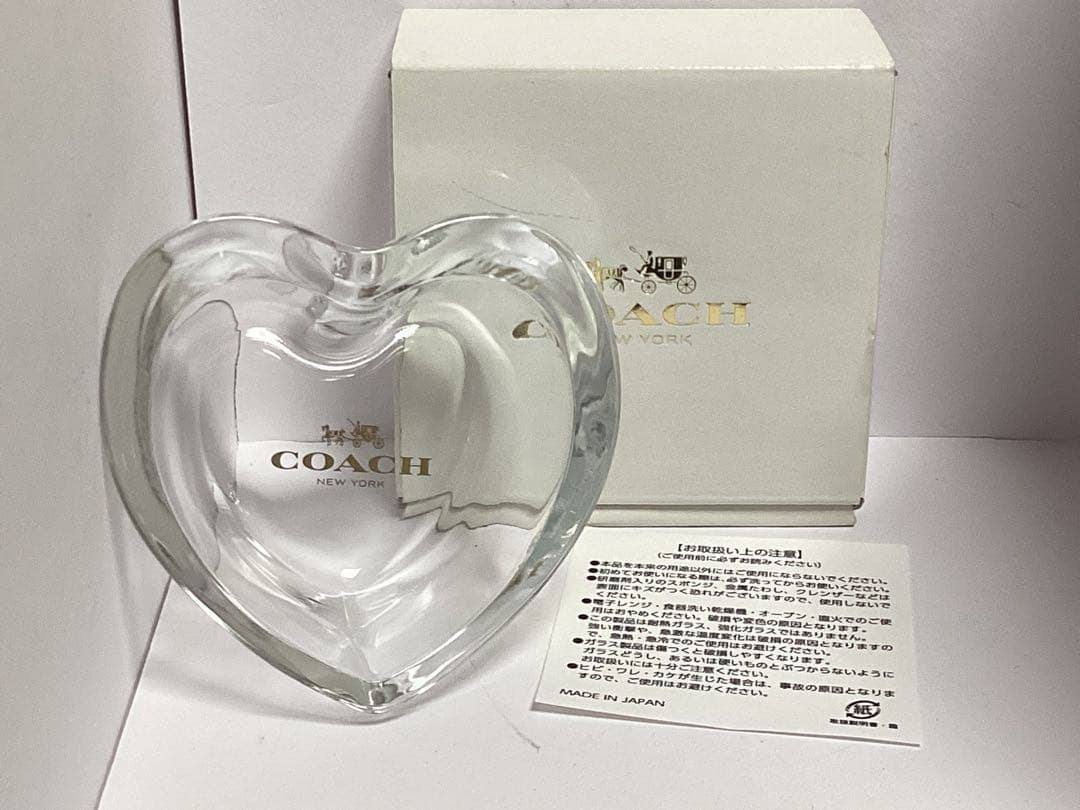 Heart-shaped glass case with a COACH logo displayed in front of its box and an instruction paper.