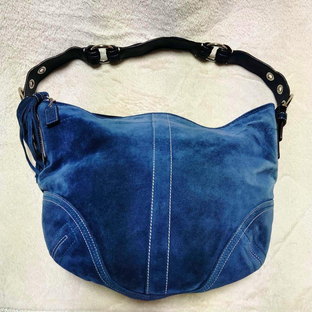 Blue suede hobo-style bag with white contrast stitching, a black leather shoulder strap, and a fringe charm laid flat on a light background.