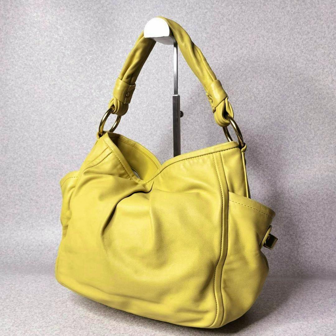 Yellow Coach hobo shoulder bag in cow leather displayed on a stand, showing the front and handle.