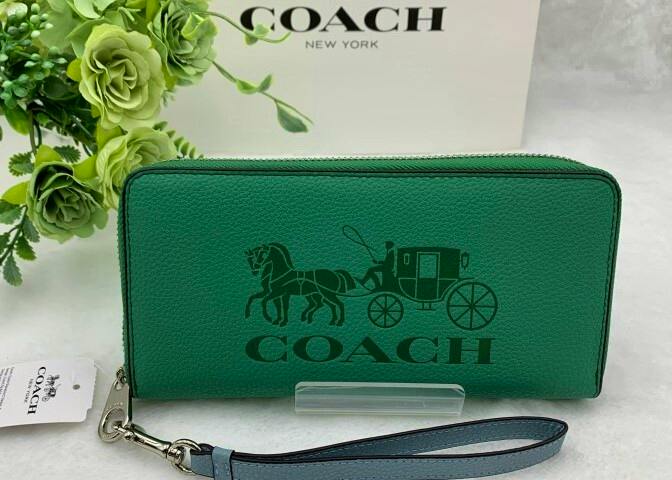 Green COACH long zip leather wallet showing embossed horse-and-carriage logo and a detachable wrist strap.