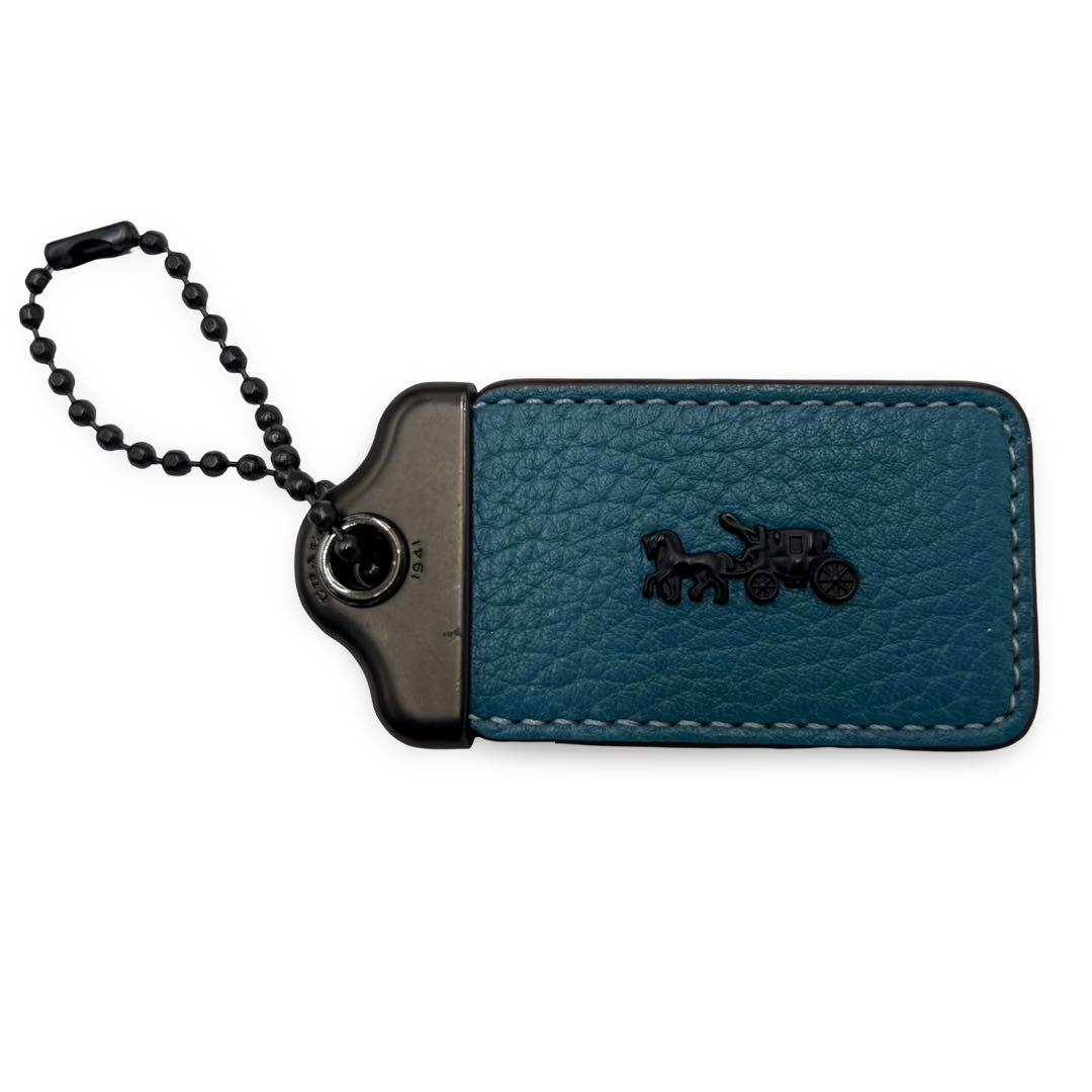 Blue cow leather COACH horse-and-carriage hangtag charm keychain with a black ball chain on a white background.