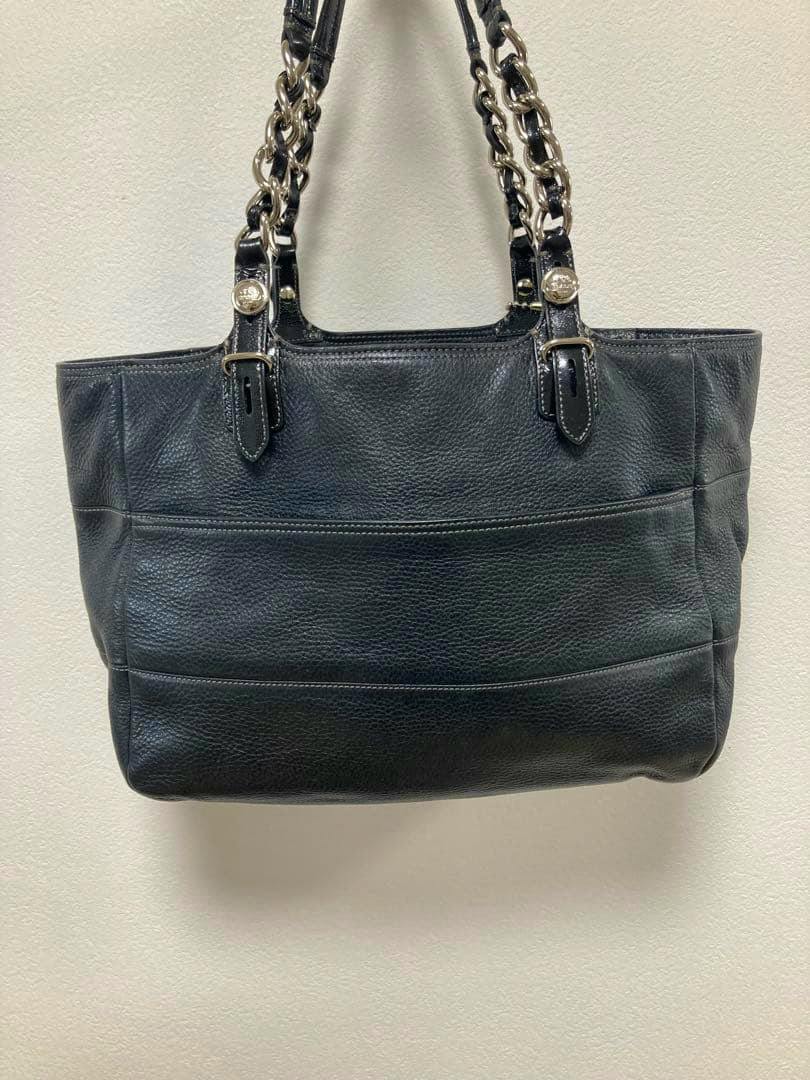 Black pebbled leather Coach chain-handle tote bag shown front-on against a plain wall.