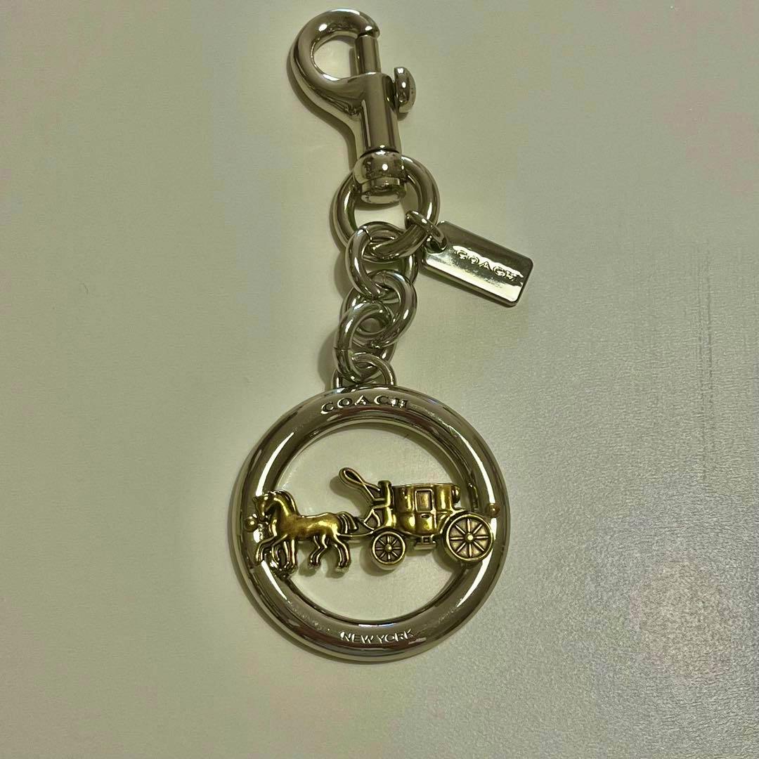 Silver COACH bag charm showing the round horse-and-carriage medallion attached to a chain and clasp.