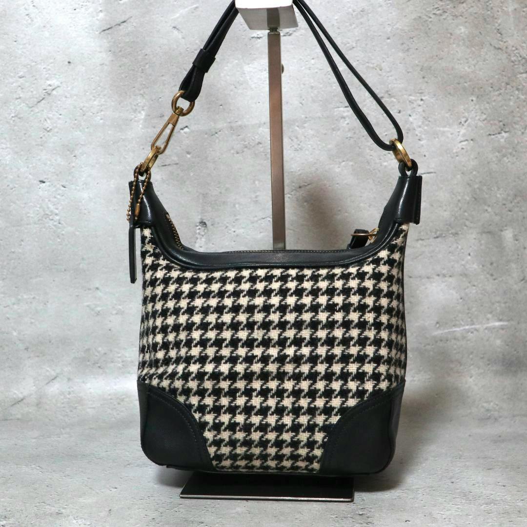 Front view of a COACH black leather‑trim houndstooth shoulder bag displayed on a stand.