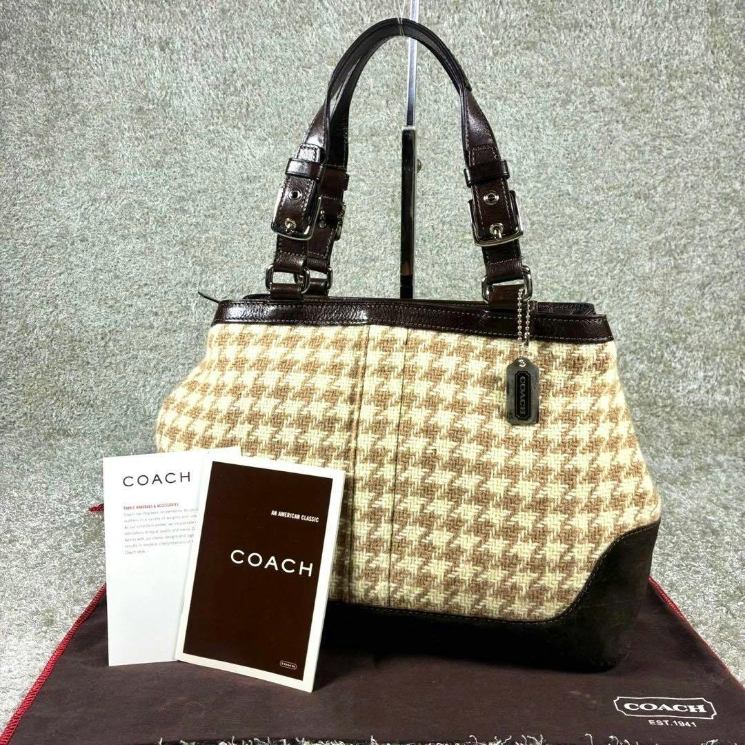 Coach houndstooth wool and suede handbag with leather handles displayed upright on a stand with Coach cards and dustbag.