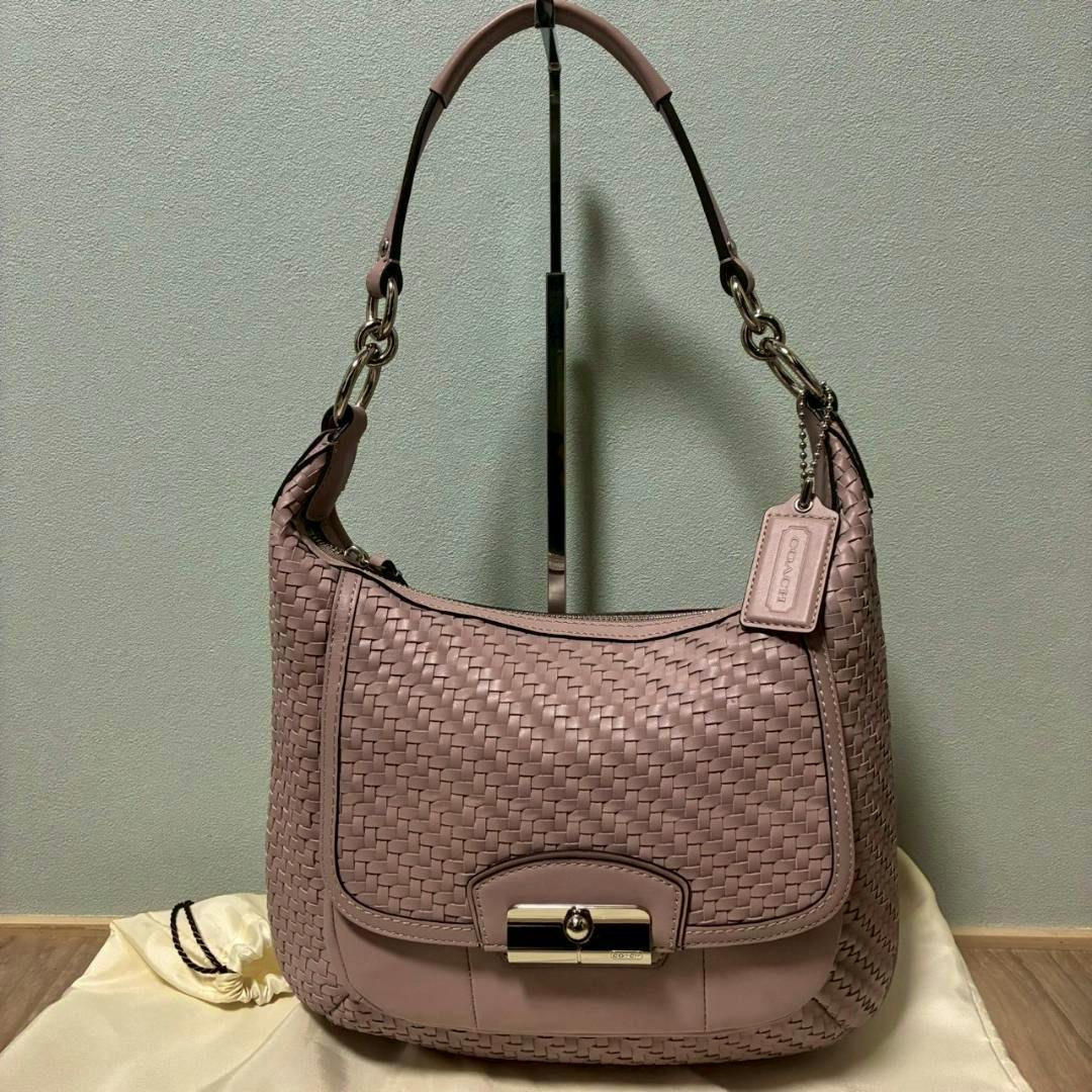 Pink COACH intrecciato leather 2-way bag hanging on a stand against a plain background.