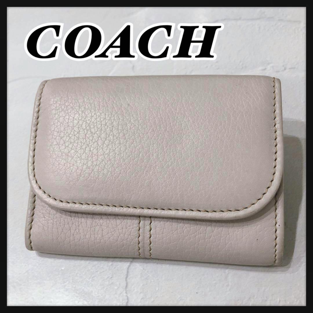 Ivory leather coin case with a flap closure and visible stitching shown on a white surface.