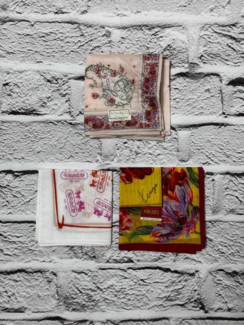 Three folded cotton handkerchiefs from a 3-piece set shown on a white brick background.