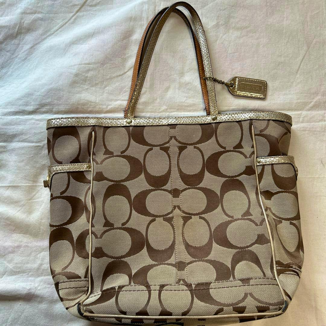 Large COACH canvas tote bag with signature C pattern, metallic-trimmed top edge, and dual leather handles shown lying flat.