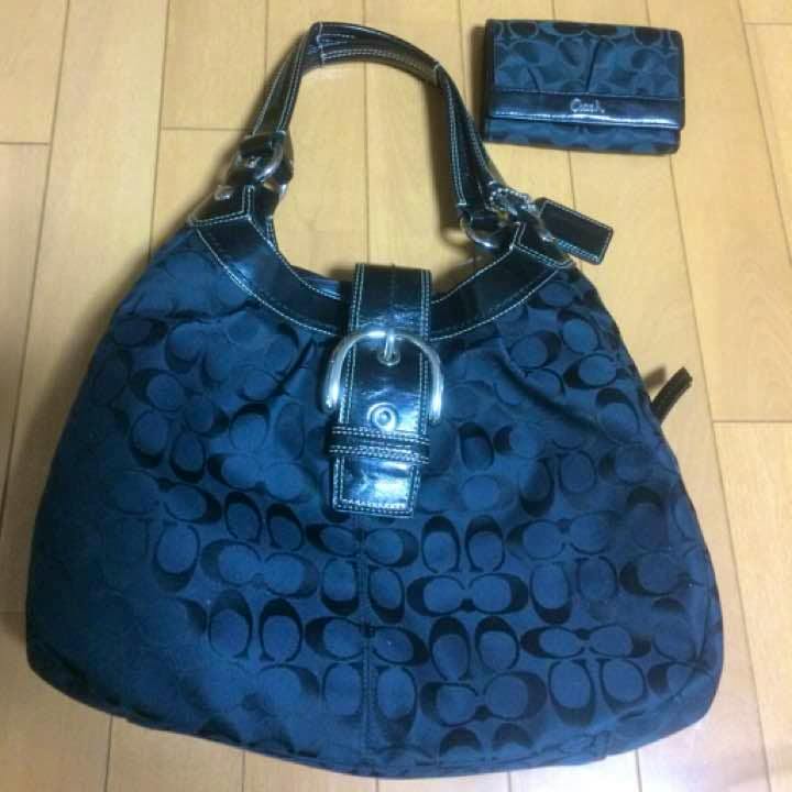 Black canvas Coach large-capacity shoulder bag with matching trifold wallet on a wooden floor.
