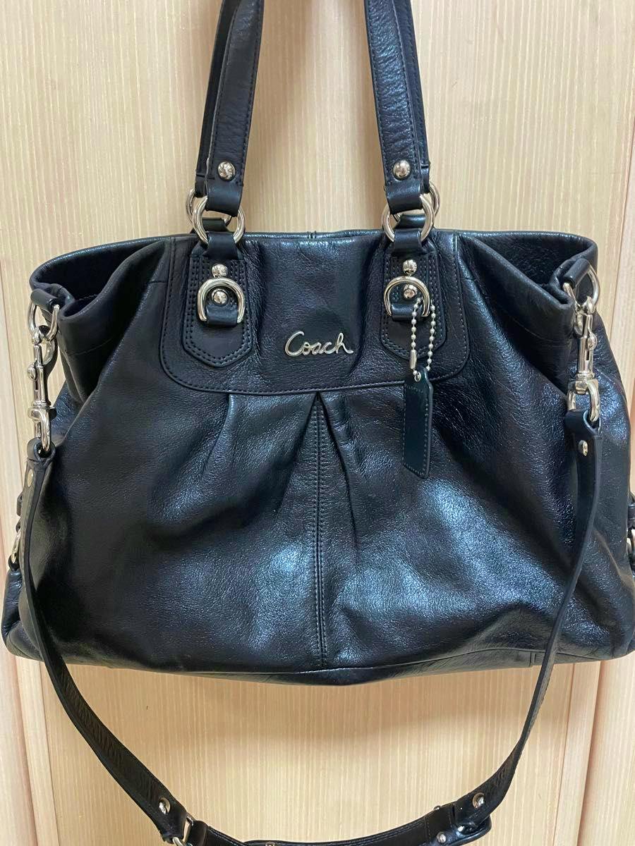 Front view of a black Coach leather 2-way shoulder handbag hanging against a wooden background.
