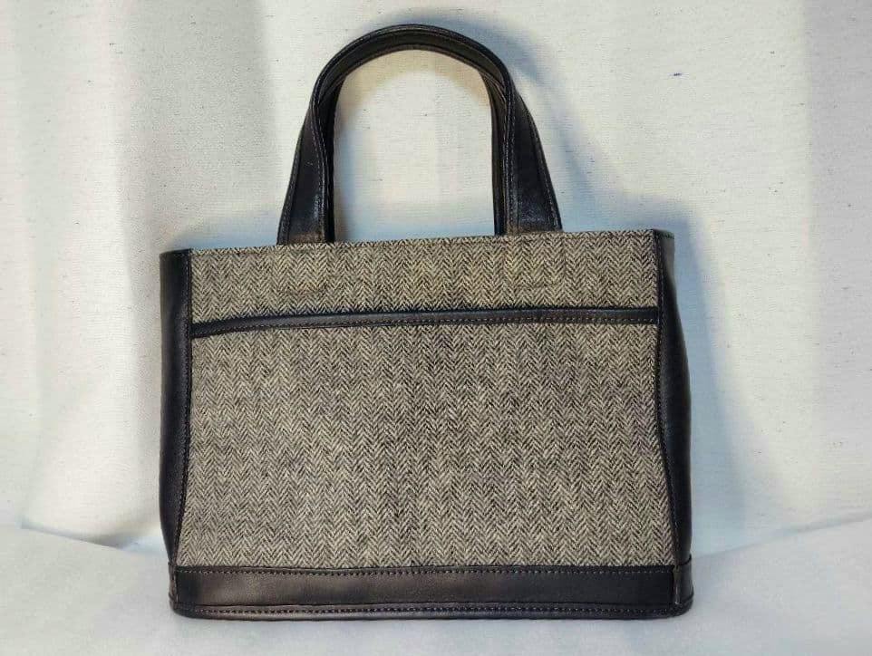 Front view of a Coach handbag in gray-black herringbone wool with black leather trim.