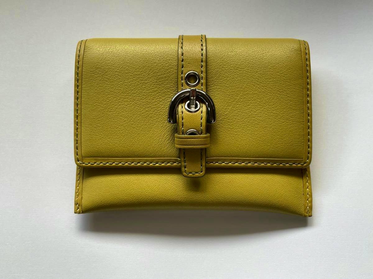 Front view of a yellow leather Coach card case with a buckle-style tab, photographed on a white background.