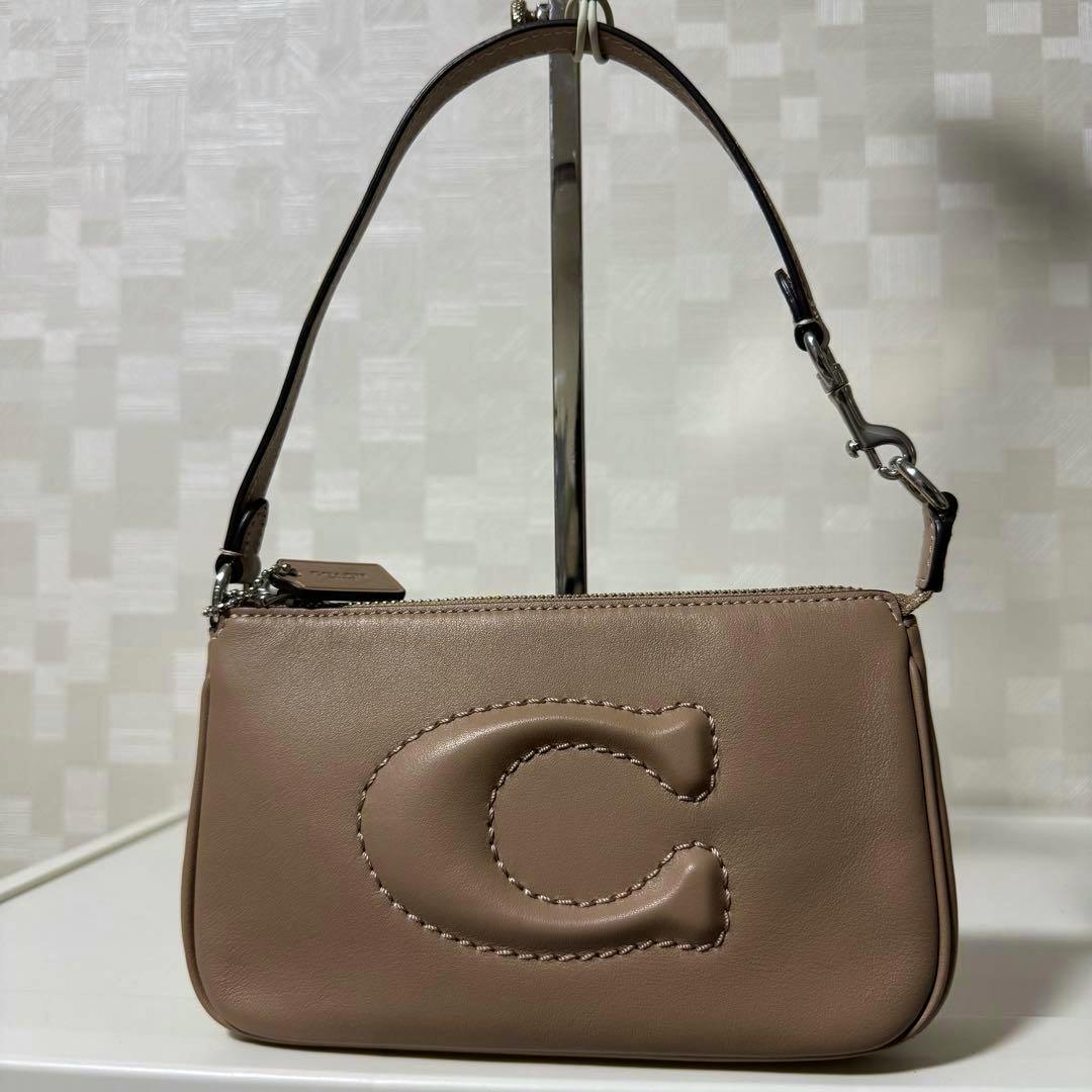 Brown leather Coach accessory pouch handbag with a stitched raised C logo and short strap against a neutral background.