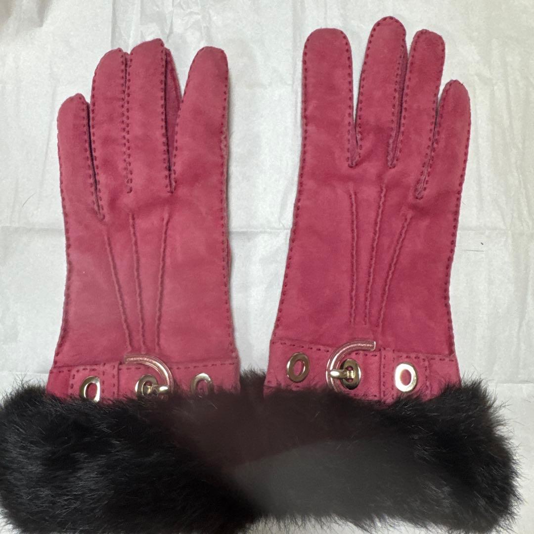 Pink suede leather women's gloves with dark fur cuffs laid flat on a light background.