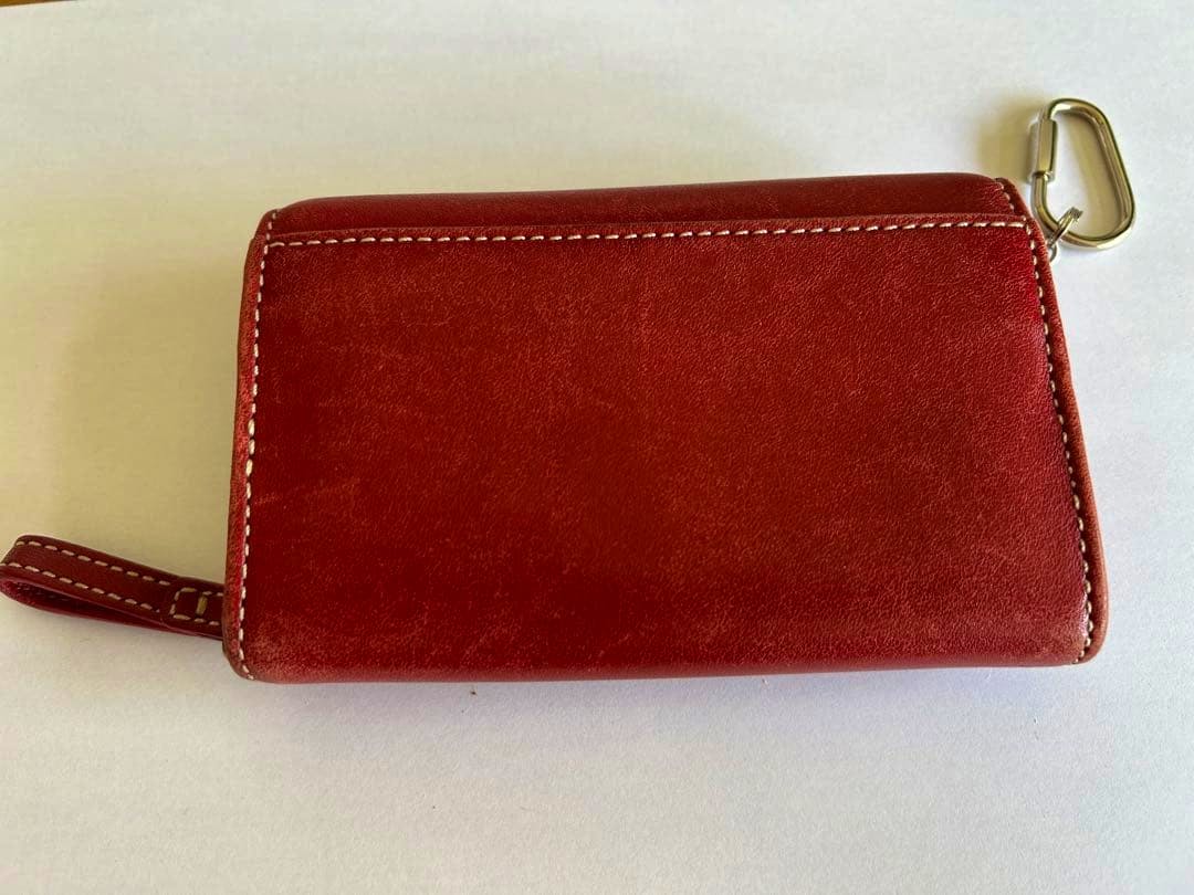 Closed red leather COACH coin case on a white background, showing stitching and a metal clasp.
