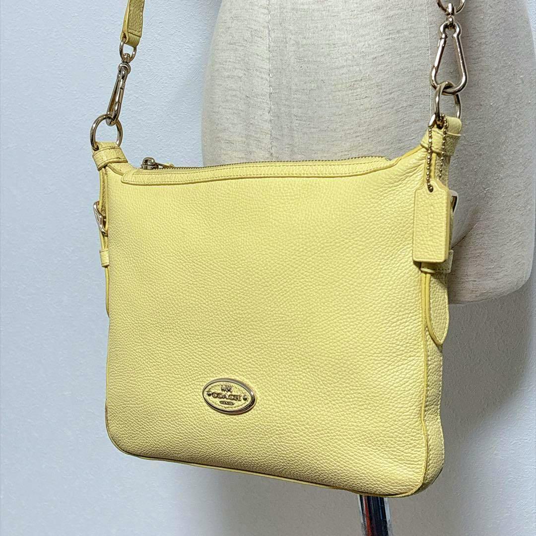 Yellow Coach leather shoulder bag hanging on a dress form, front view showing the logo and strap.