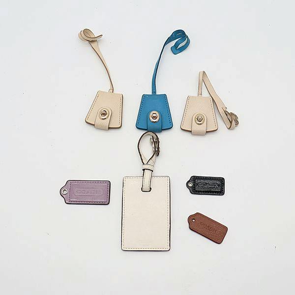 Seven Coach luggage tags and keychain charms arranged on a white background, including a rectangular white leather luggage tag and six smaller colored leather tags.